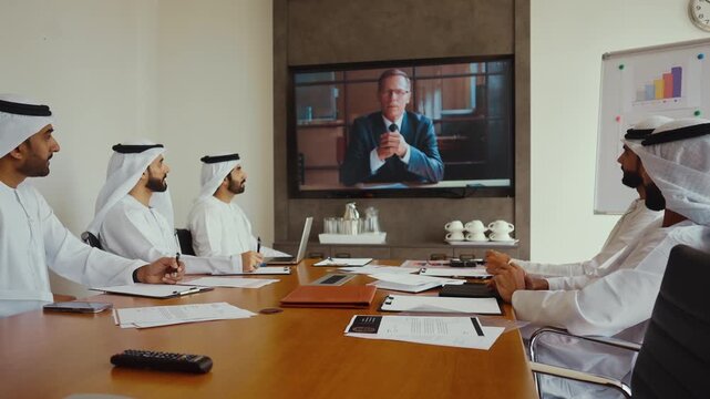 Emirati businessmen in traditional attire video conferencing with a european partner in a modern office, discussing investment, strategy and international corporate collaboration