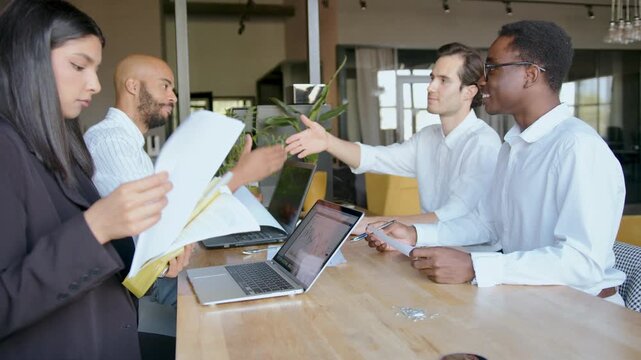 Four colleagues discuss financial issues in an office space. One man shakes hands with another to show agreement, highlighting teamwork and collaboration in a professional environment
