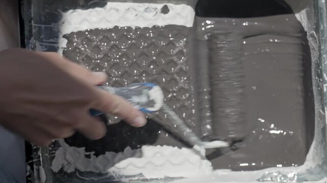 Close up of paint roller dipped in paint and rolled across tray surface. Concept of painting preparation, renovation, and DIY decorating