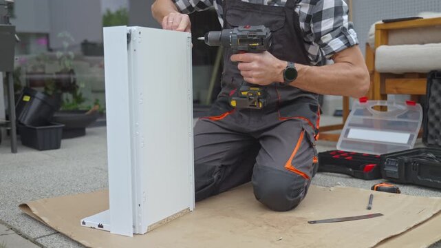 Man inserts screw into drawer panel and drives it with cordless drill at an assembly workspace. Concept of DIY furniture assembly and repair