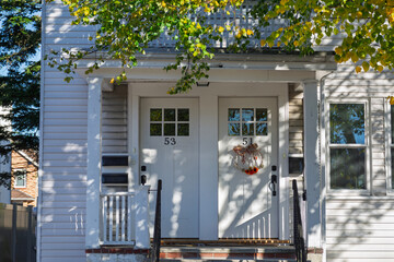 Naklejka premium White duplex house entrance with autumn wreath and dappled sunlight in Boston neighborhood 