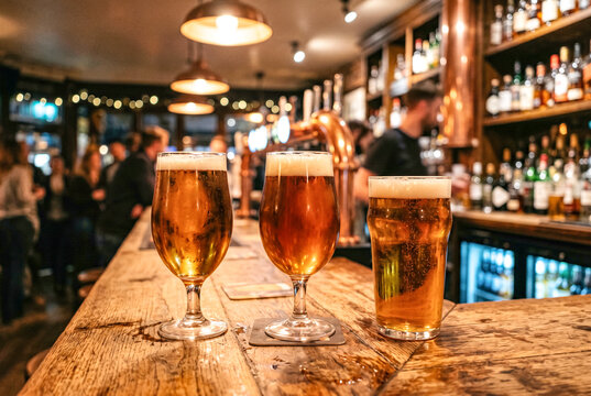 木製カウンターに並ぶ三杯のビールがあるパブ
