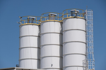 Obraz premium Large Industrial Storage Silos Against Clear Blue Sky in Manufacturing Facility