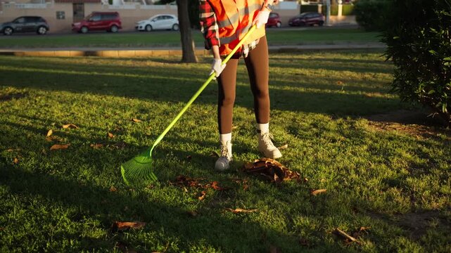 Female municipal park worker wearing orange safety vest cleaning public park, maintaining green urban spaces and supporting city cleanliness and environmental care.