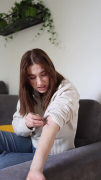 Vertical screen Young woman removing tick from arm with tweezers after dangerous insect bite while checking skin inflammation and symptoms of tick borne infection