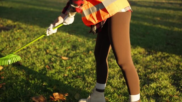 Female environmental worker in safety vest cleaning public park, promoting sustainability, environmental responsibility, and care for urban green spaces.