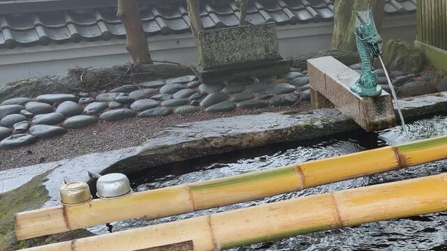 Traditional tsukubai stone fountain stands in a temple yard. This stone basin is located at Raizan Sennyoji Daihioin temple grounds in Fukuoka, Japan. 