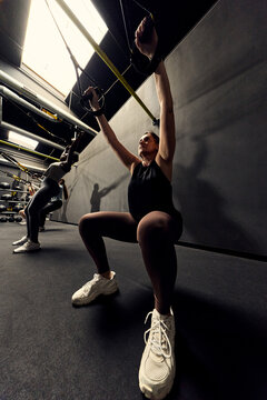 Women doing suspension training squats in a gym focusing on fitness, strength and determination. 