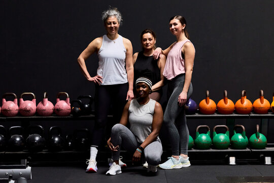 Four diverse women posing confidently in a gym with kettlebells and workout gear