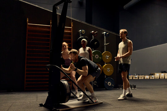 Group fitness training in a gym with diverse athletes coached during an intense workout session. The vibe is energetic, and everyone is smiling and sweaty. They are cheering each other on.