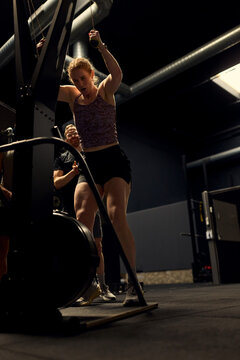 Female athlete pushing through intense gym workout with coach support during functional fitness training session