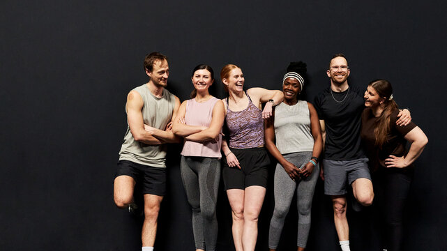 Smiling diverse fitness group of friends and teammates posing together after a workout. They stand side by side, with a good atmosphere between them. Smiling and laughing.