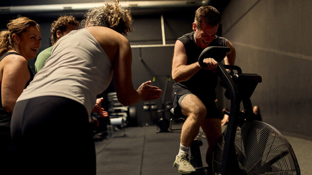Men and women push through an intense indoor cycling workout with teammates cheering in a dark gym