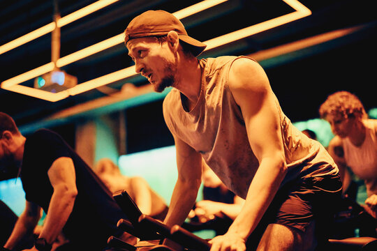 Focused man pushing through intense spin class workout in neon-lit gym group cycling session