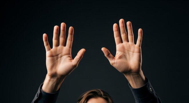 Human hands raised in surrender, signaling a plea for help or an expression of fear against a dark background.