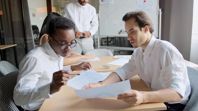 Two men discuss financial charts in an office meeting to plan future strategies for business growth and improve performance while a third person observes and participates