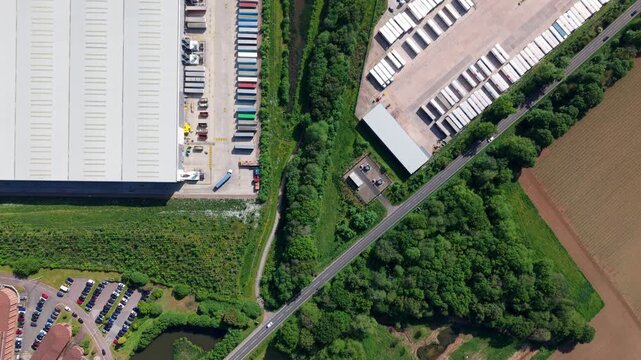 High angle drone view of a major logistics fulfillment center with commercial freight trucks docked at distribution bays.