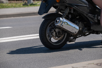 Fototapeta premium Black Motor Scooter Wheel and Exhaust Riding Through Urban Street Traffic