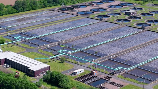 Drone perspective looking down at circular primary sedimentation tanks, final settlement clarifiers, and massive anaerobic digestion domes at the Minworth wastewater treatment facility near Birmingham
