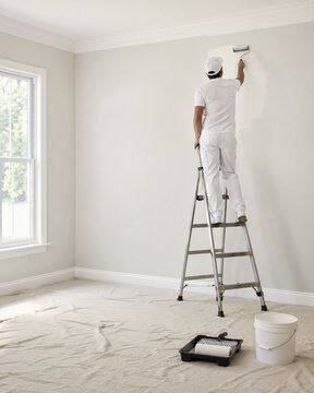 Pintor em escada pintando parede alta de ambiente interno