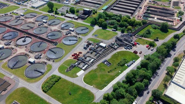 Drone perspective looking down at circular primary sedimentation tanks, final settlement clarifiers, and massive anaerobic digestion domes at the Minworth wastewater treatment facility near Birmingham