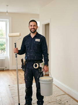 Pintor profissional com balde e rolo em ambiente reformado