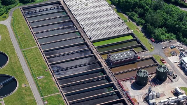 Drone perspective looking down at circular primary sedimentation tanks, final settlement clarifiers, and massive anaerobic digestion domes at the Minworth wastewater treatment facility near Birmingham