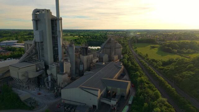 High angle aerial drone view of a massive industrial cement factory and manufacturing plant bathed in golden light at sunset in Rugby Warwickshire UK
