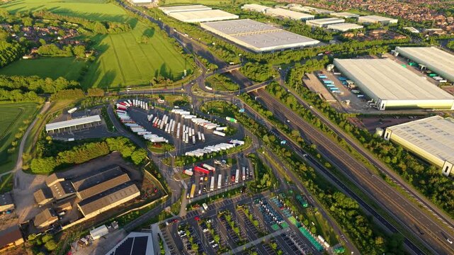 High angle drone view of a major motorway service area showing commercial truck transport yards and public vehicle parking layouts in Rugby, UK.
