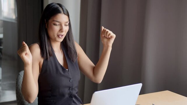 Indian woman celebrates success while dancing in an office after completing a project with joy and happiness in front of her laptop