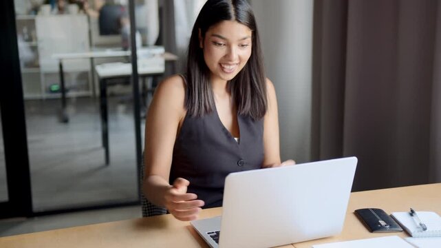 An Indian woman joyfully celebrates the successful completion of her project in the office, working on her laptop with the modern office in the background