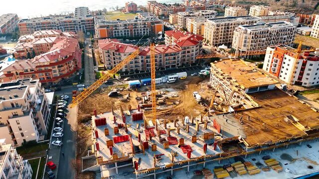High angle view of concrete pouring at building construction site. Aerial view of tower crane and workers on concrete structure with red formwork at residential project site.