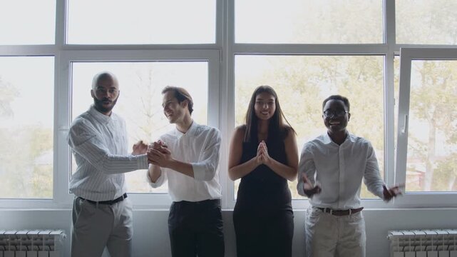 Four colleagues stand by a window in an office, celebrating their success together. They give each other high fives and express joy, creating a friendly environment
