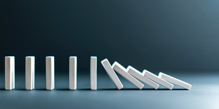 White domino blocks falling in chain reaction on dark surface