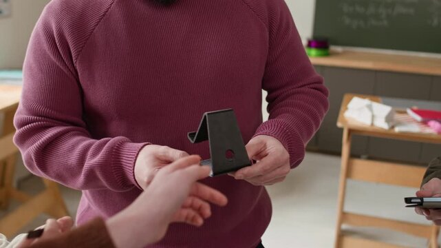 High angle close up shot of unrecognizable male teacher showing 3D printed plastic item to students during school modeling class