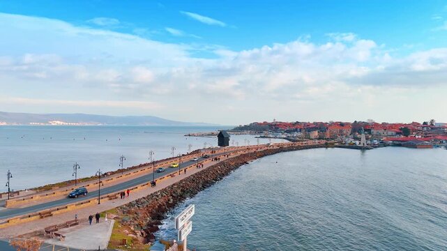 Aerial view of causeway bridge leading to Nessebar old town. High angle view of a road bridge over the sea with a traditional wooden windmill connecting to a peninsula.