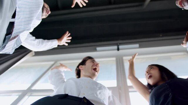 Four diverse colleagues come together in a spirited huddle, lifting their hands in celebration of teamwork and unity. The energy is palpable as they share moments of joy and support in the office