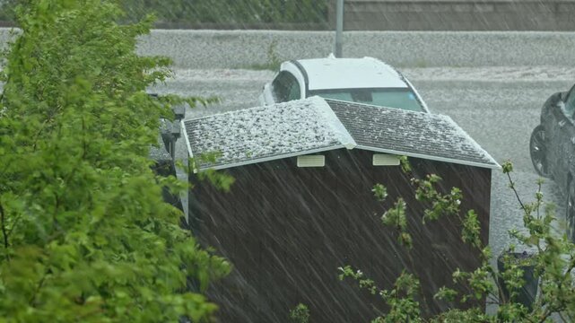 Close up view of severe hailstorm and heavy rain falling on rooftop cars and residential street. Sweden.
