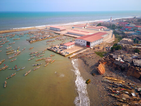 Aerial view of James Town fishing harbor with traditional wooden boats and industrial warehouses along the coast in Accra, Greater Accra Region, Ghana.