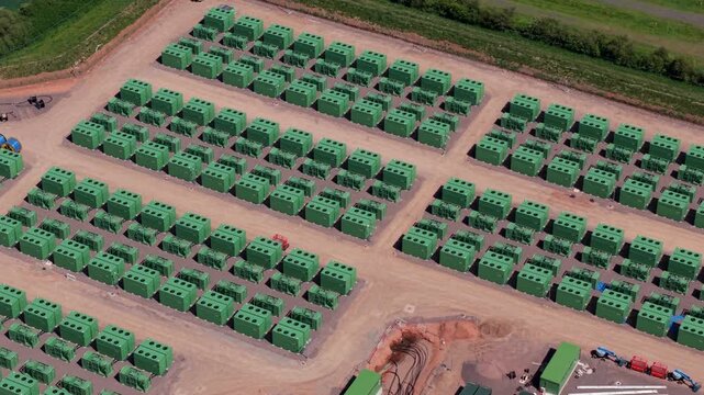 High angle aerial drone view of a large battery energy storage system BESS facility with rows of green containerized power modules for grid stability in Coleshill Warwickshire UK