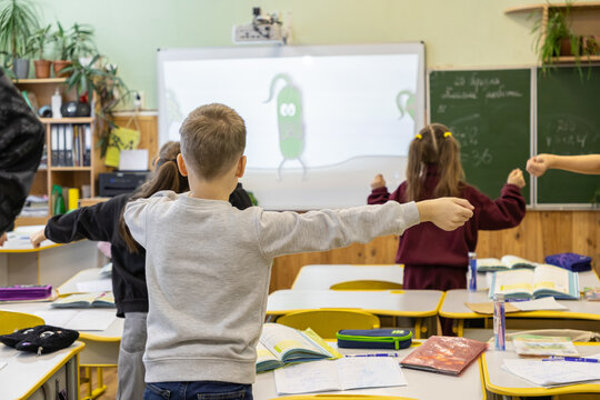 Elementary school children perform physical exercises during class to promote active learning and student wellness within a modern classroom featuring a digital screen and chalkboard