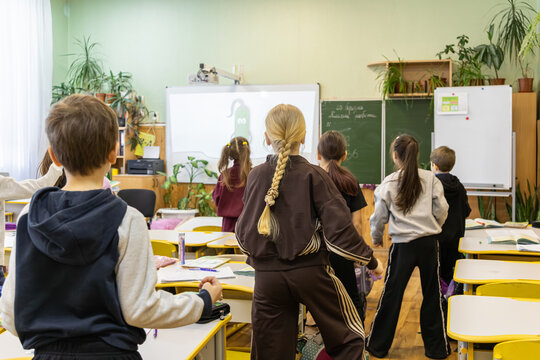 Elementary school children stand at desks during an interactive lesson for a group physical break activity that encourages movement and focus in a modern classroom setting for pupils