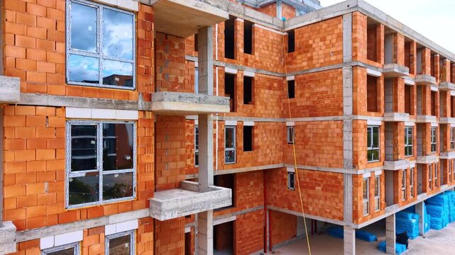 Multi story residential building under construction with ceramic brick walls. Close up view of apartment building construction site with installed windows and orange brickwork