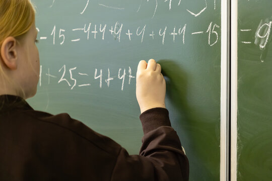 A dedicated elementary school student solves a complex math equation on a green chalkboard to demonstrate academic progress, learning development, and achievement in the classroom