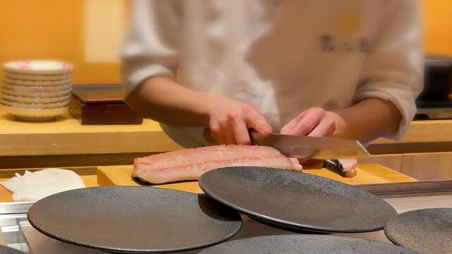 Professional Japanese sushi master slicing fresh raw tuna fish fillet on wooden cutting board in Tokyo. Experienced chef using authentic single bevel yanagiba knife to make cuts for premium sashimi.
