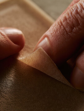 Biodegradable pad wrapper closeup hands peeling paper seal natural skin texture warm light macro detail