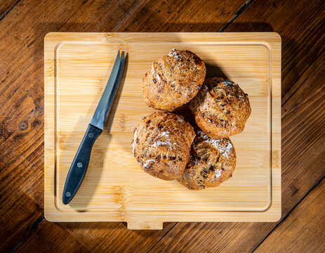 Four classic farm country bread buns on a wooden chopping board next to a cheese knife. These homemade rustic rolls balls are made of organic wholemeal multigrain wheat flour for a sourdough recipe.