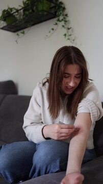 Vertical screen Young woman removing tick from inflamed arm with tweezers while showing growing danger of parasite bites and rising seasonal infection risks