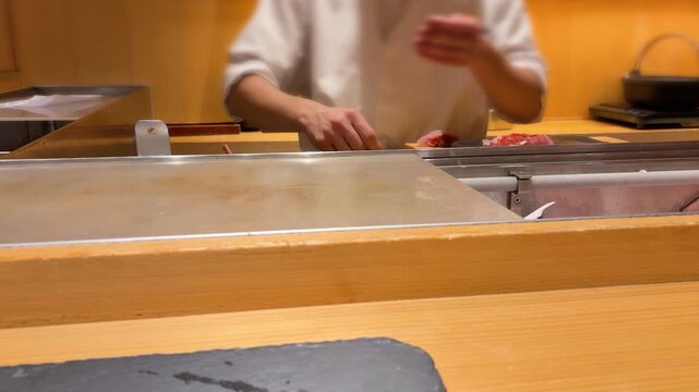 Professional sushi chef preparing fresh tuna fillet at traditional restaurant counter. Hands of Japanese master slicing and seasoning dark red raw fish. Premium omakase dining experience.