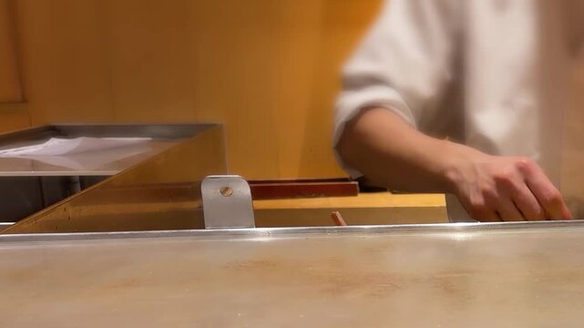 Professional sushi chef preparing fresh tuna fillet at traditional restaurant counter. Hands of Japanese master slicing and seasoning dark red raw fish. Premium omakase dining experience.